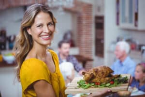 mature female in yellow dress holding a platter of roast chicken for her family