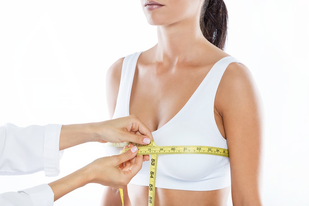 doctor measuring chest of woman in white sports bra with measuring tape