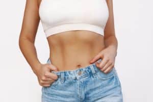 Cropped shot of young tanned slender woman in denim shorts with toned stomach with abs